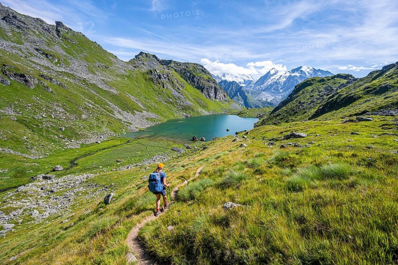 Mountaineer on hiking trail in picturesque mountain landscape, view of mountain lake Lac du Louvie and glaciated mountain peaks of the Grand Combine, Valais Alps, Val de Bagnes, Valais, Switzerland