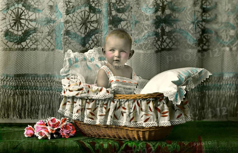 Baby in a basket, 1920s, A toddler sits cosily in a bassinet, surrounded by floral details, Historical photo