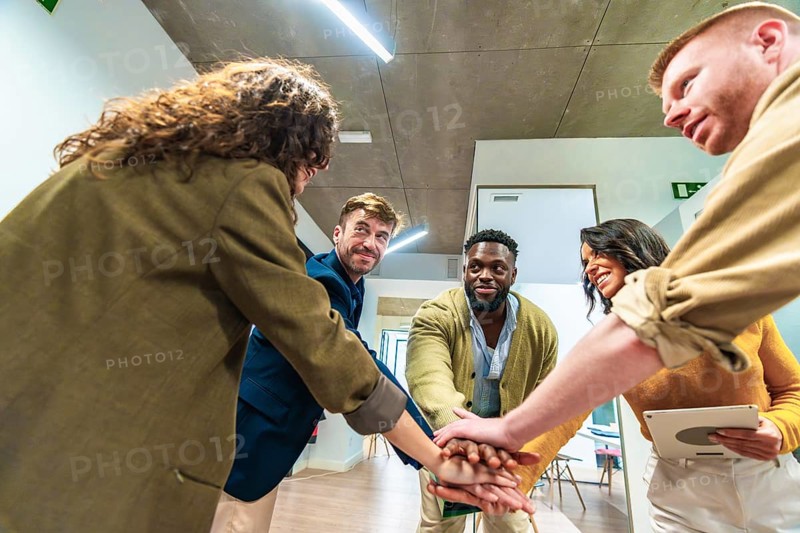 Five businesspeople joining hands together in office, showing their unity and cooperation for a common goal