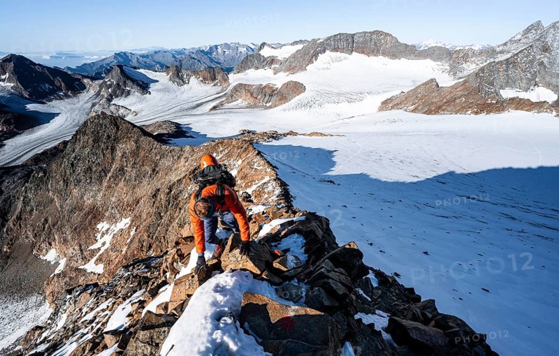 Mountaineer climbing on a rocky ridge on the mountain peak Wilder Freiger, in the background Signal summit and summit of Becher with Becherhaus, picturesque high mountain landscape, view of glacier Übeltalferner and rocky mountain peaks Königshofspitz and Sonklarspitze, Stubai Alps, South Tyrol, Italy