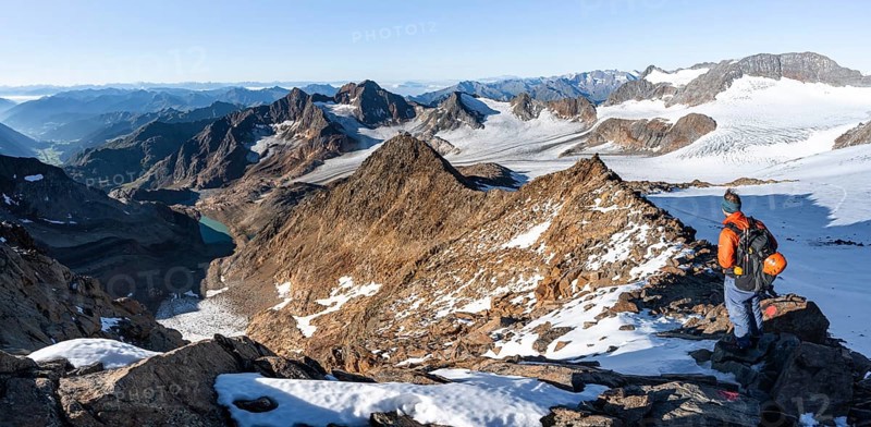 Mountaineer on a rocky ridge on the Wilder Freiger summit, behind him Signal summit and Becher summit with Becherhaus, picturesque high mountain landscape, view of Übeltalferner glacier and rocky mountain peaks Königshofspitz and Sonklarspitze, Stubai Alps, South Tyrol, Italy