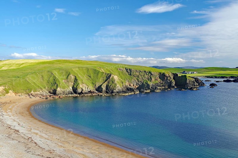 Green hills hug a sandy coastline with calm blue waters and wide open skies, Hillswick, Eshaness, Shetland Islands, Scotland, United Kingdom