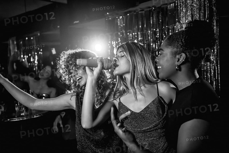 Group of friends singing joyfully during karaoke night, enjoying each other's company and creating unforgettable memories in a lively nightclub