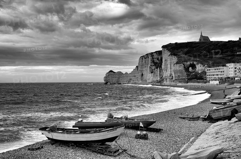 Boats lying on the beach, pebble beach, rock arch Falaise or Porte d'Amont, church Chapelle Notre Dame de la Garde, Étretat, sea, steep coast, cliffs, chalk cliffs, alabaster coast, La Côte d'Albâtre, black and white, Normandy, Seine-Maritime, France