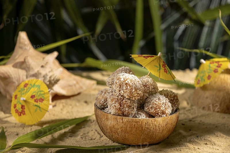 Coconut, bowl filled with sweet confectionery on sand, decorated with yellow umbrellas