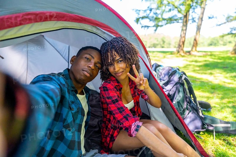 Young couple taking a selfie inside their tent while camping in nature, enjoying a relaxing vacation