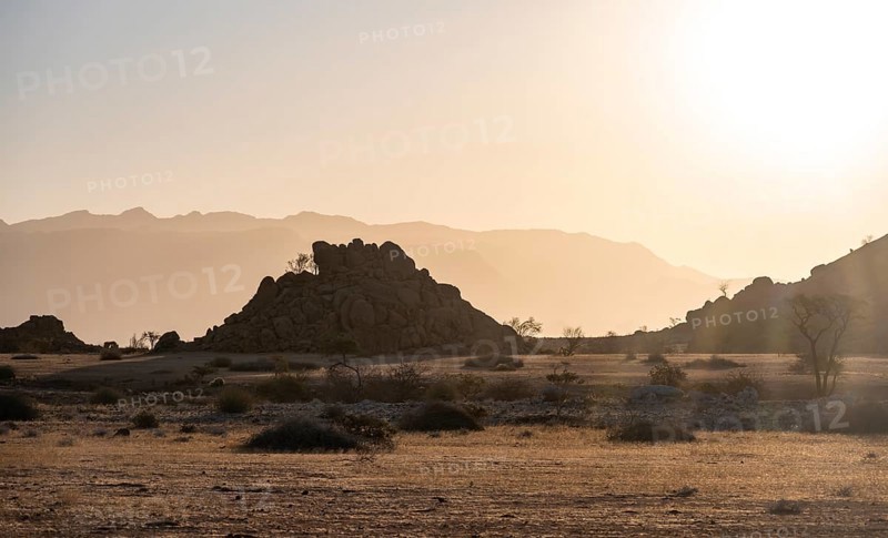Desert landscape in the evening light at sunset, barren landscape with hills of stacked rocks, backlit, Brandberg in the background, Erongo, Damaraland, Namibia