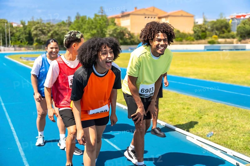 Group of athletes catching their breath and recovering after completing a race on a vibrant blue track, celebrating their achievements together