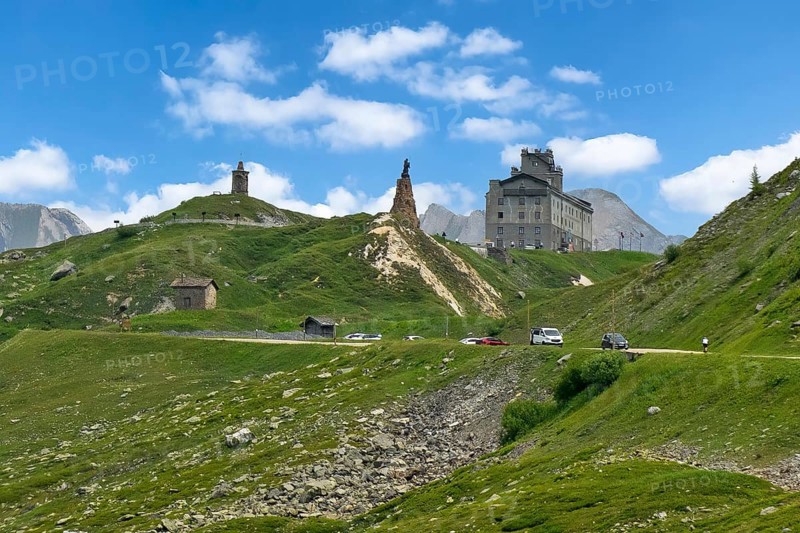 View from south on pass summit of Colle del Piccolo San Bernardo, Col du Petit Saint Bernard Little Saint Bernard Pass in Alps with on the right historic renovated reopened Hospice Hospice in the centre statue of monk Saint Bernard of Menthon on large pedestal of natural stones, Département Savoie, France