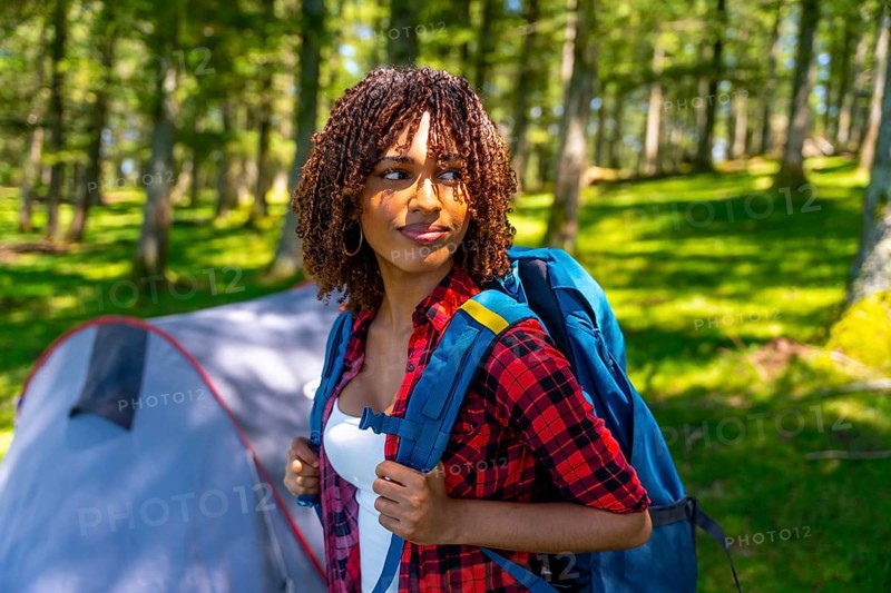 Young woman with a backpack enjoying the tranquility of a forest, discovering nature while camping near a cozy tent on her adventure