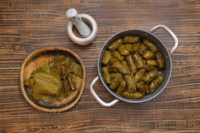 Delicious dolma is being prepared at home, featuring grape leaves wrapped around a savory filling. The cooking pot is filled with neatly arranged rolls, showcasing traditional culinary skills