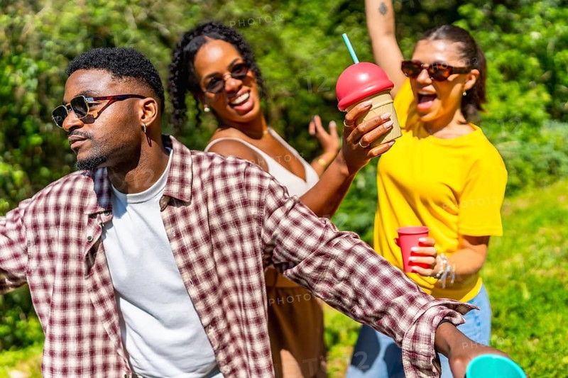 Three friends enjoying summer sunshine, dancing joyfully while sipping cold drinks and sharing laughter in a vibrant outdoor setting