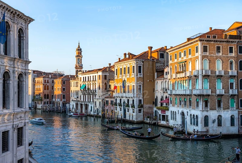View of the Grand Canal with gondoliers at sunset, picturesque evening mood with palazzos on the canal and church tower of the Chiesa Parrocchiale dei Santi Apostoli, view from the Rialto Bridge, Venice, Veneto, Italy