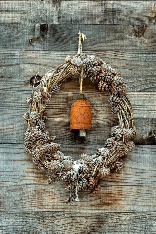 A wreath made of pinecones and natural materials is displayed on a rustic wooden wall. An antique bell adds a charming touch, Aubrac region, Occitanie.France