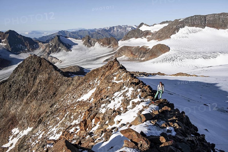 Mountaineer on a rocky ridge on the Wilder Freiger mountain peak, behind signal peak and Becher peak with Becherhaus, picturesque high mountain landscape, view of Übeltalferner glacier and rocky mountain peaks Königshofspitz and Sonklarspitze, Stubai Alps, South Tyrol, Italy