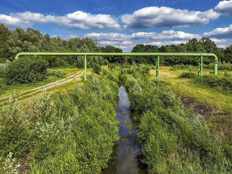 Bottrop, North Rhine-Westphalia, Germany - Renaturalised Boye, the tributary of the Emscher, has been transformed into a near-natural watercourse, flood protection through newly designed flooding areas, the Boye is now free of wastewater following the construction of a parallel sewer, is part of the Emscher river system and thus part of the Emscher conversion, was previously an open, above-ground wastewater channel, mixed water channel with surface water and wastewater. Wind turbine on the Mottbruch spoil tip at the back