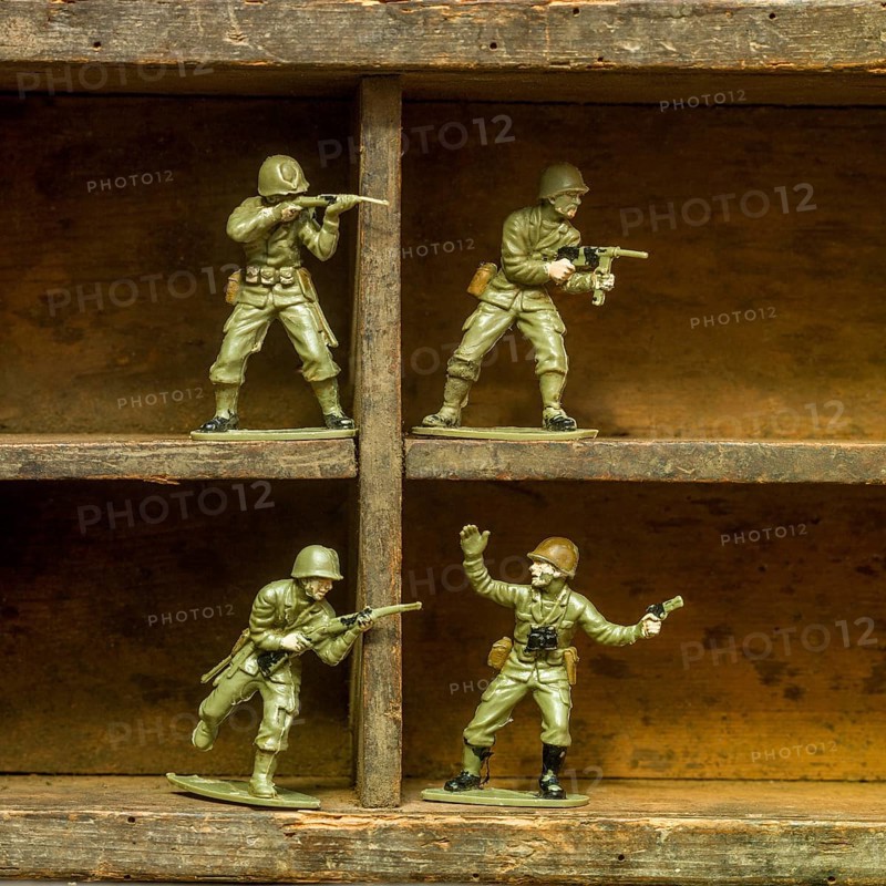 A set of classic plastic toy soldiers arranged on a wooden shelf, displaying soldiers in various action poses with rifles and gear, illustrating a playful military theme