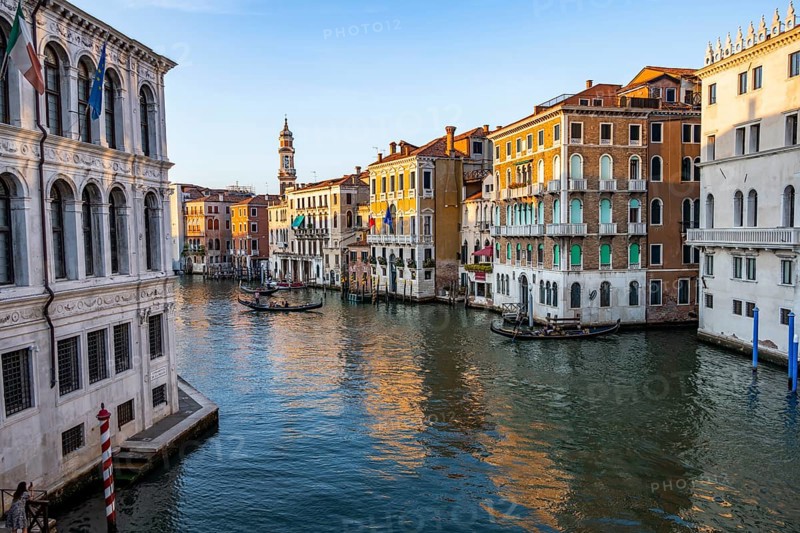 View of the Grand Canal with gondoliers at sunset, picturesque evening mood with palazzos on the canal and church tower of the Chiesa Parrocchiale dei Santi Apostoli, view from the Rialto Bridge, Venice, Veneto, Italy
