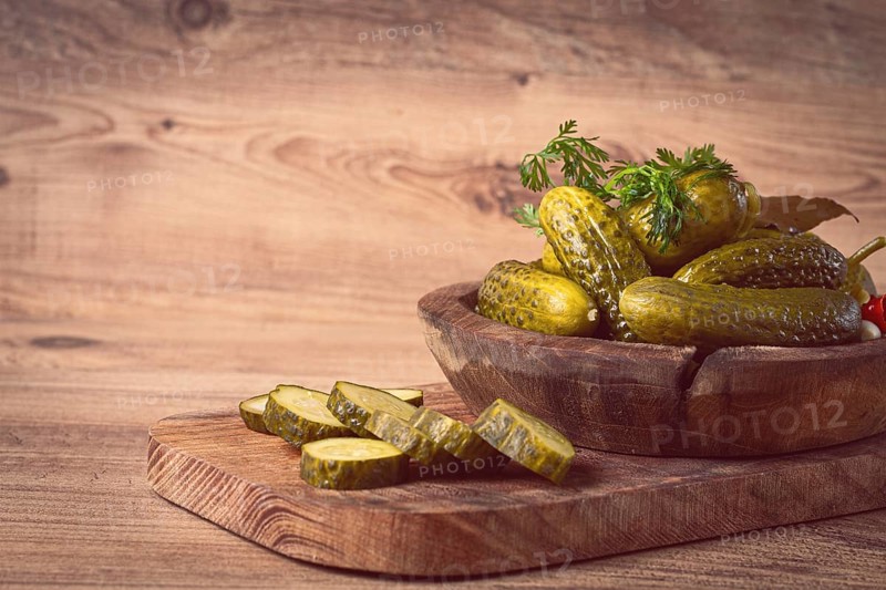 Pickled cucumbers in a wooden bowl with herbs and spices, close-up, rustic style