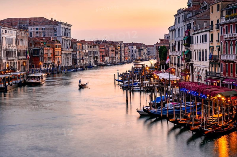 View of the Grand Canal with gondoliers at sunset, picturesque evening mood with illuminated palazzos on the canal, long exposure, view from the Rialto Bridge, Venice, Veneto, Italy