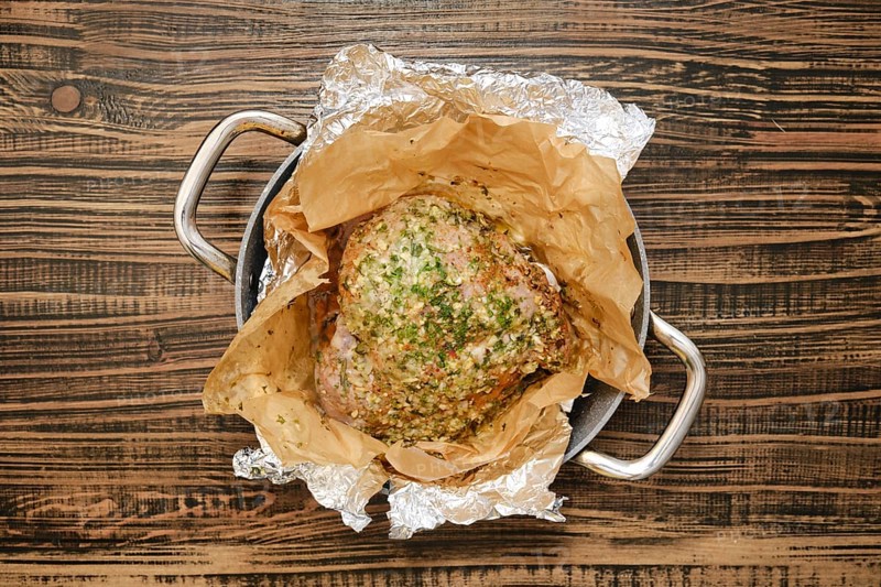 A perfectly roasted turkey thigh, seasoned with herbs and spices, rests on a bed of parchment paper inside a roasting pan. The warm, golden skin glistens, inviting a festive feast
