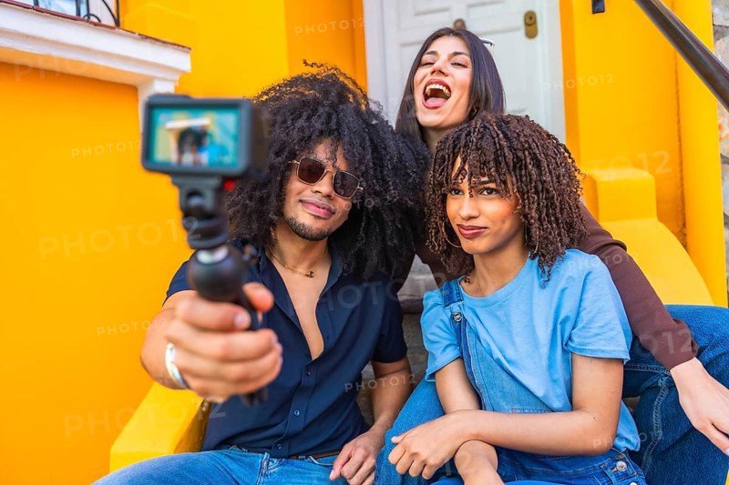 Three latin friends filming a vlog using a gimbal and action camera, enjoying laughter and smiles while sitting on vibrant yellow steps