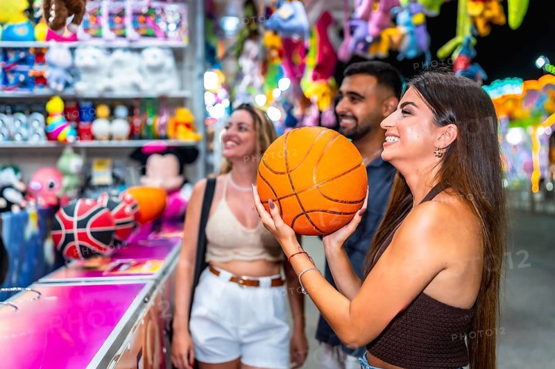 Group of friends enjoying a lively evening at a funfair game stall, celebrating their basketball win with laughter and smiles