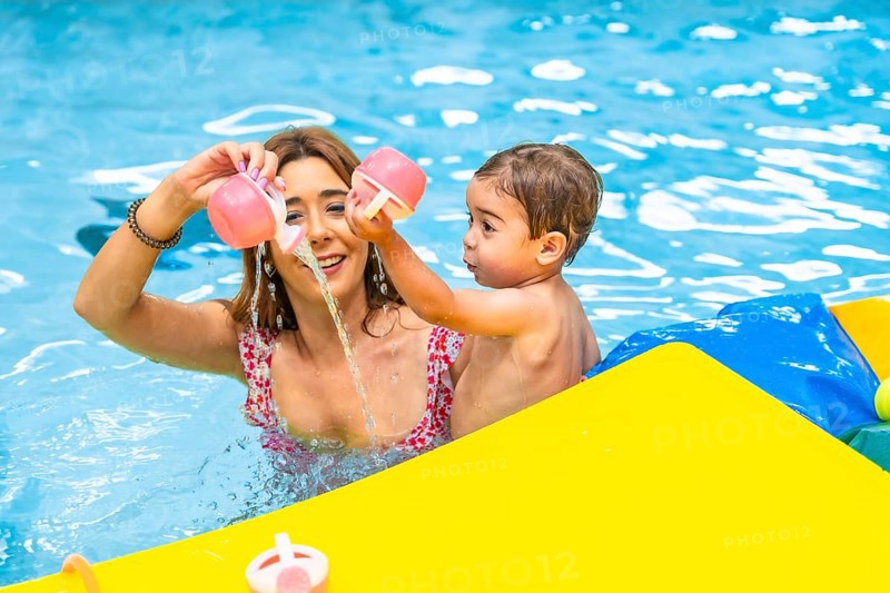 Mother and son enjoying playtime together, pouring water from pink toys in a bright yellow inflatable boat, creating a cheerful summer scene