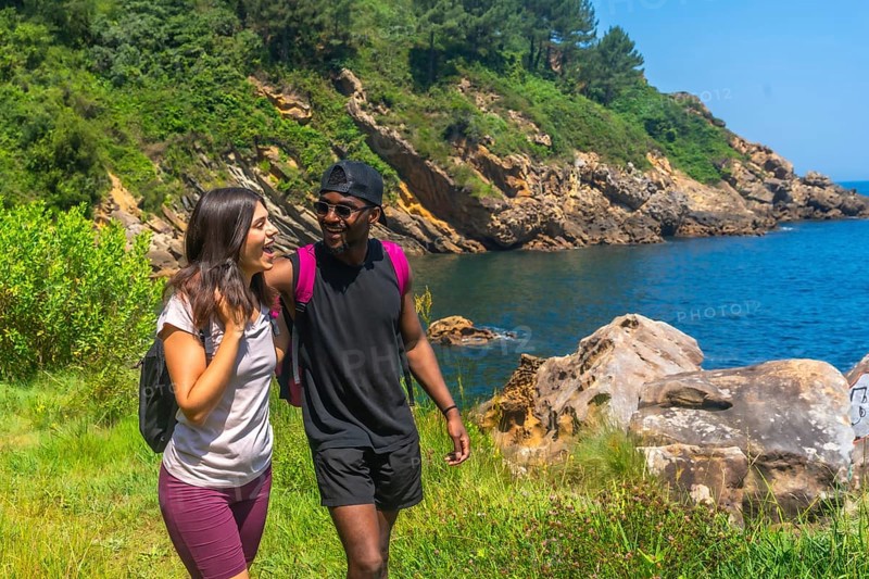 Young couple walking and laughing along a beautiful coastline path on a sunny summer day, enjoying the scenic views