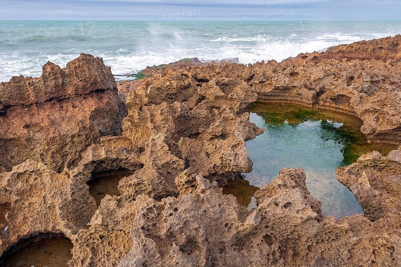 A rocky area with a hole in the ground. The hole is filled with water. The water is brown in colour. Rabat, Morocco