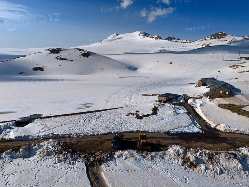 Huts and a road embedded in snow-covered mountains under a clear blue sky, aerial view, Aragaz, Aragac, Alagyaz, extinct stratovolcano, 4090 m, Aragazotn, Shirak, Armenia