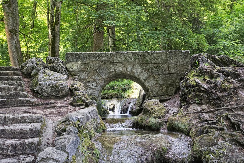 An old, small stone bridge over the Brühlbach, wild and romantic stream and source of the Urach waterfall in a dense forest, Bad Urach