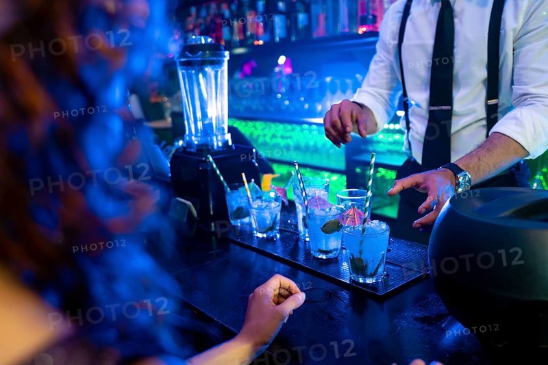 Bartender skillfully preparing vibrant blue cocktails garnished with fresh mint and ice in a lively nightclub atmosphere
