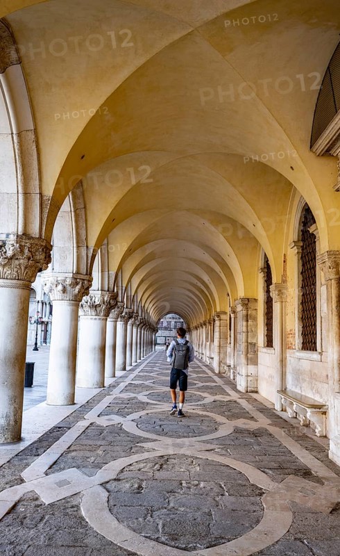 Young man walking through the portico of the Doge's Palace, St Mark's Square, Venice, Veneto, Italy