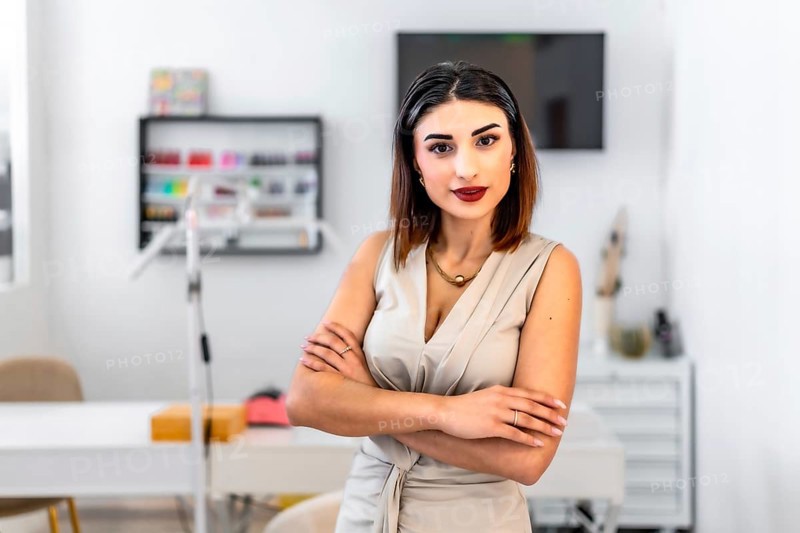 Young female entrepreneur posing with crossed arms in her hair and beauty salon, looking confident and professional