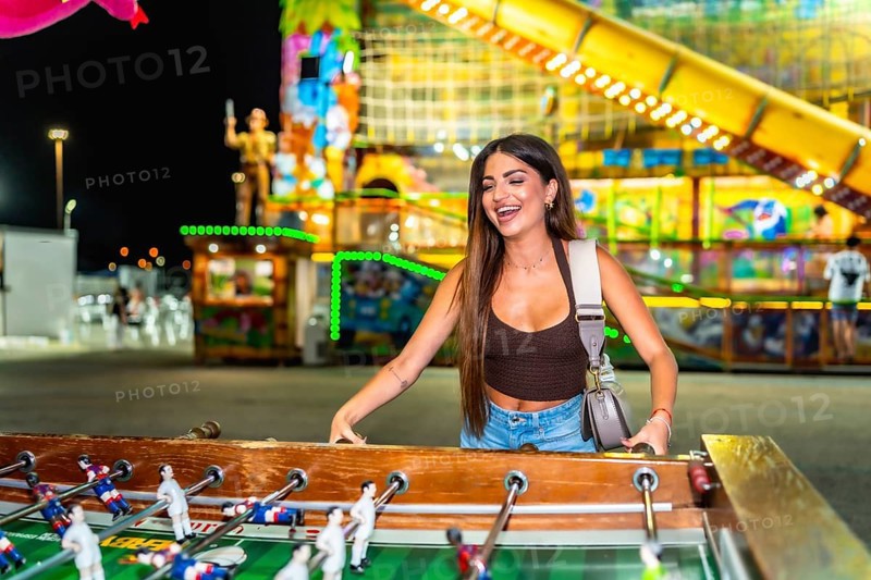 Happy young woman enjoying a vibrant evening at a funfair, playing table football and soaking up the festive atmosphere