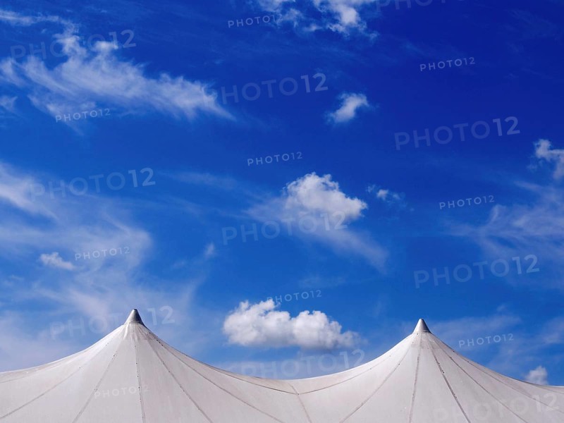 Exhibition tent under a bright blue sky adorned with fluffy clouds in a lively outdoor setting