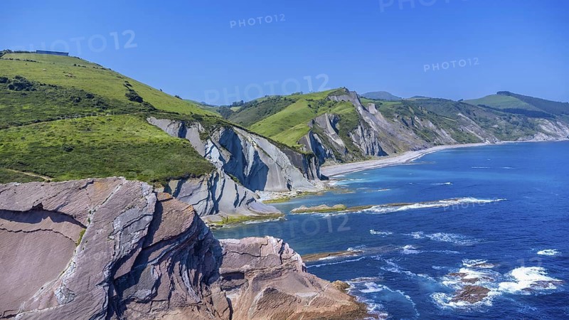 Breathtaking aerial view of the iconic zumaia flysch cliffs meeting the vibrant turquoise waters of the bay of biscay on a sunny summer day, Spain.
