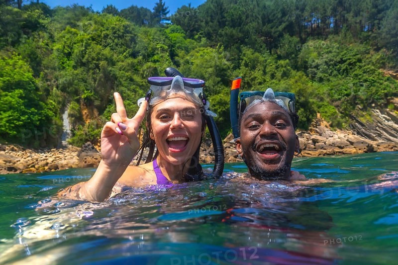 Young multi ethnic couple enjoying snorkeling together in crystal clear tropical sea, woman making victory sign