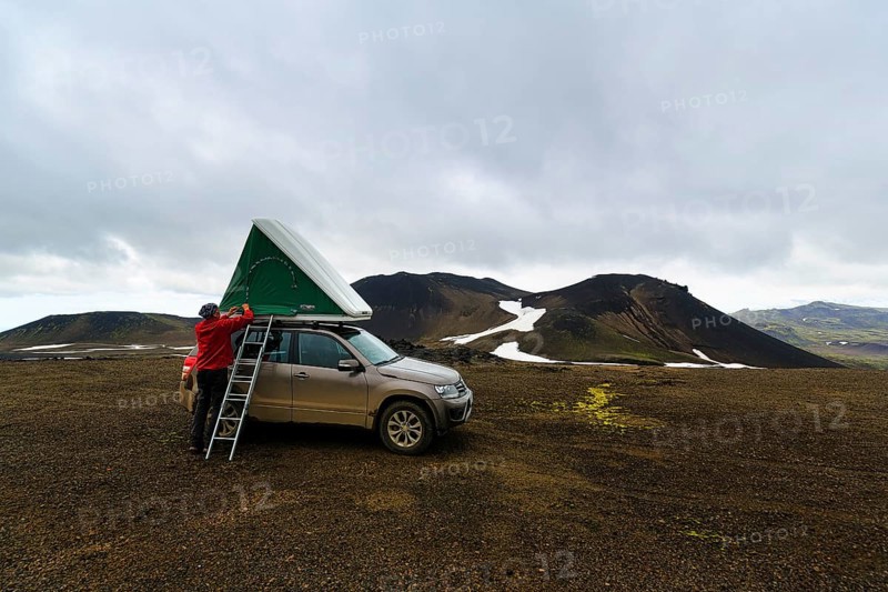 Barren volcanic landscape with snowfields, off-road vehicle with roof tent and ladder on mountain peak, camping, rain clouds, Snaefellsjökull, Snæfellsnes peninsula, Snaefellsnes, West Iceland, Iceland