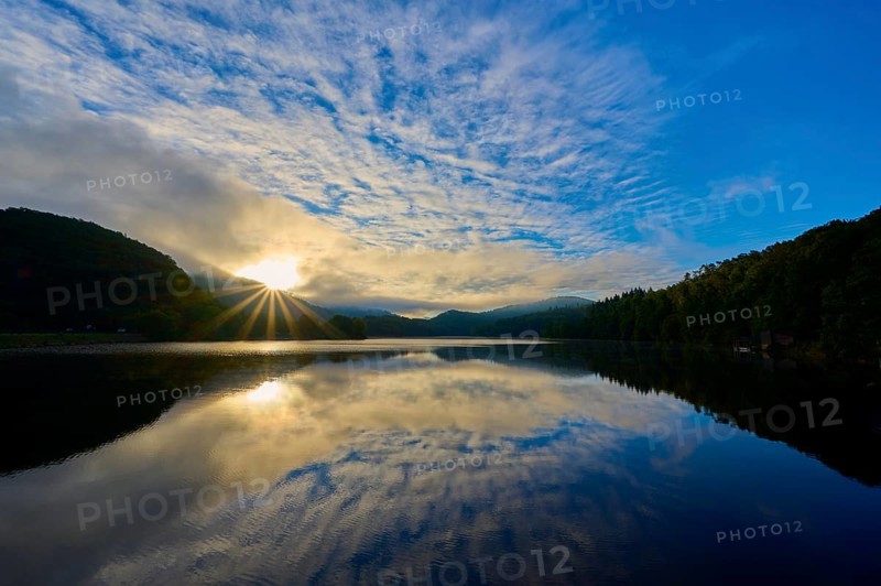 Sunbeams break through clouds and are reflected in a calm lake surrounded by green mountains, summer, Rursee, Obersee, Rurberg, Simmerath, Eifel National Park, Eifel, North Rhine-Westphalia, Germany