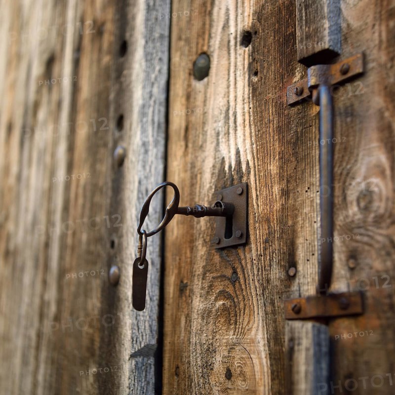 Close-up view of a rustic wooden door featuring a vintage lock and key. The texture of the wood and metal gives a classic charm, highlighting craftsmanship and history. Auvergne. France
