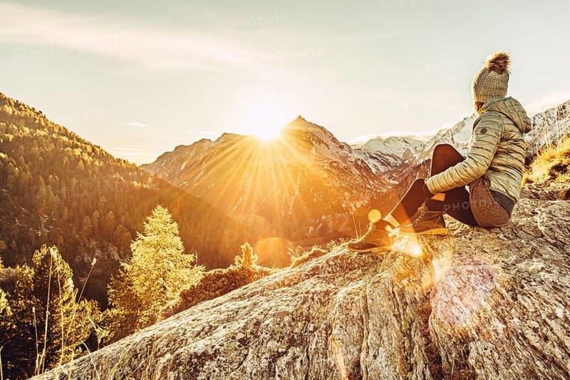 Woman sitting thoughtfully at a feslen at autumn atmosphere during sunset in the Swiss Alps in the Engadine. Photographed from the village of Maloja on the Maloja Pass