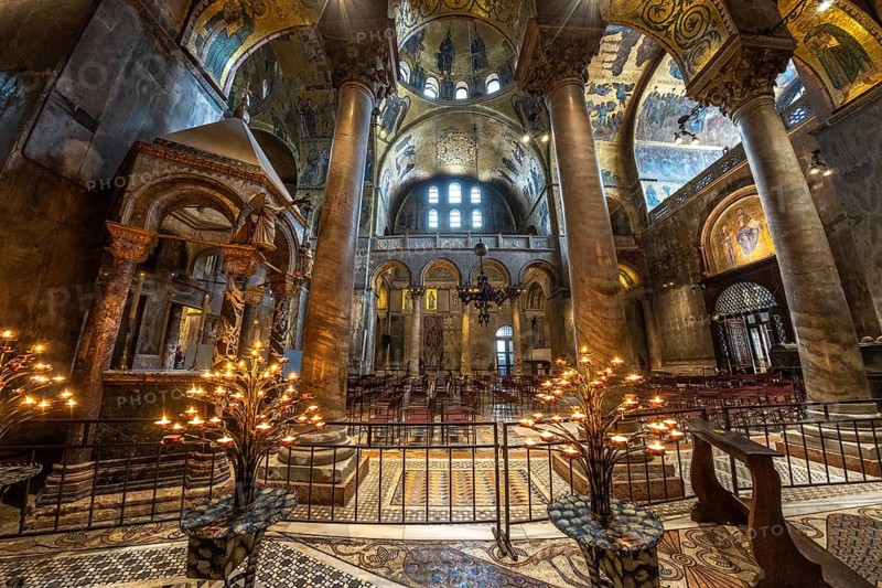 Lit candelabras illuminate the mosaic decorations and marble columns inside saint mark's basilica in venice, italy