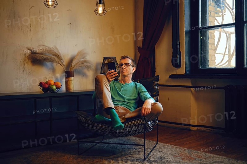 A middle-aged man sits in a chair and looks at the smartphone screen. He made an online order and checks the stage of delivery procedure