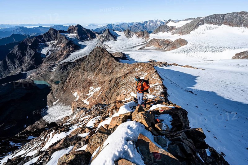 Mountaineer on a rocky ridge on the Wilder Freiger summit, behind him Signal summit and Becher summit with Becherhaus, picturesque high mountain landscape, view of Übeltalferner glacier and rocky mountain peaks Königshofspitz and Sonklarspitze, Stubai Alps, South Tyrol, Italy