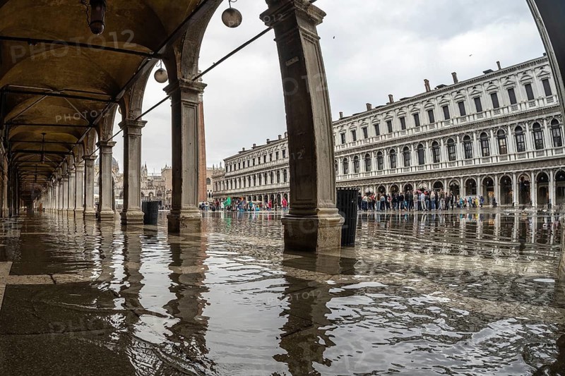 Tourists visiting piazza san marco in venice, italy, despite the rain causing flooding under the arches