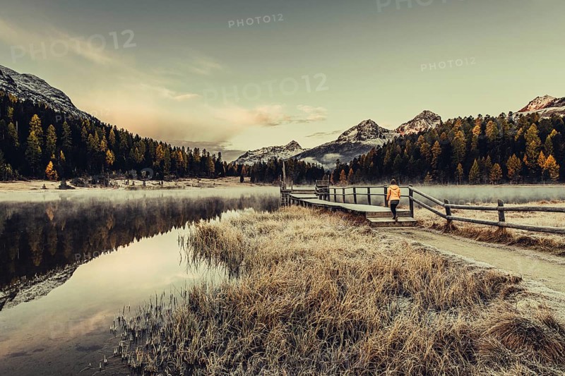 Young woman at Lake Staz near Sankt Moritz in the Engadine in Switzerland. Morning atmosphere with fog in autumn. Reflection of water