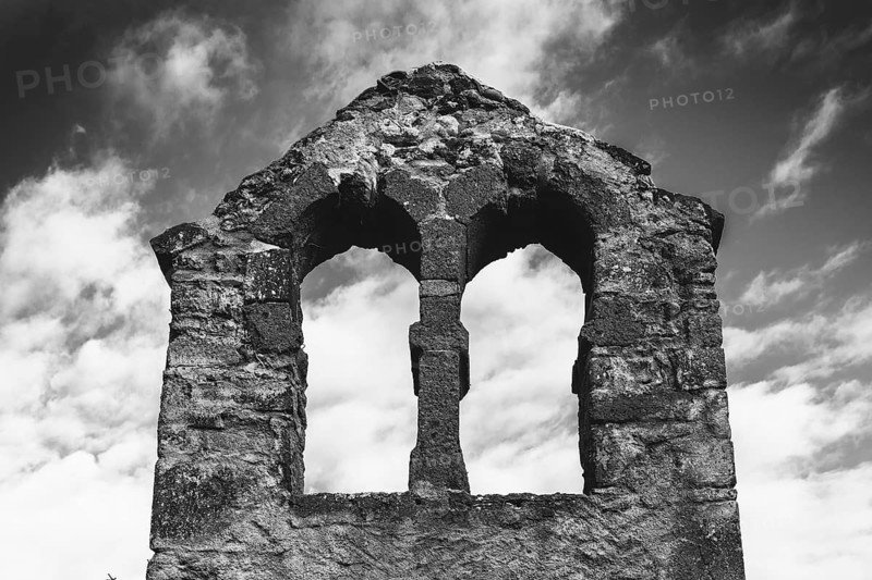 Crumbling stone ruins of a bell tower stand against a cloudy sky, showcasing two arched windows. Puy de Dome. Auvergne Rhone Alpes. France