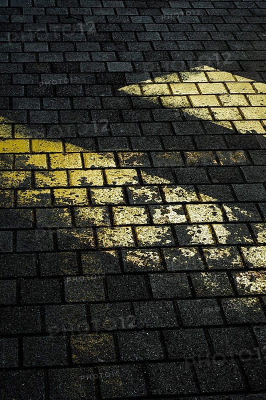 Faded yellow markings on dark, textured stone pavement create a striking contrast. The uneven surface suggests wear and age, showcasing an outdoor environment in low light